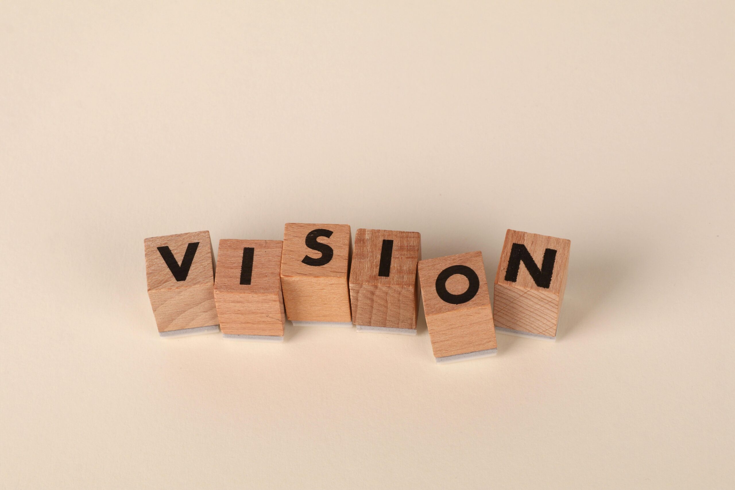 Home Wooden blocks with black letters spelling 'VISION' on a light beige background, symbolizing foresight and goals.