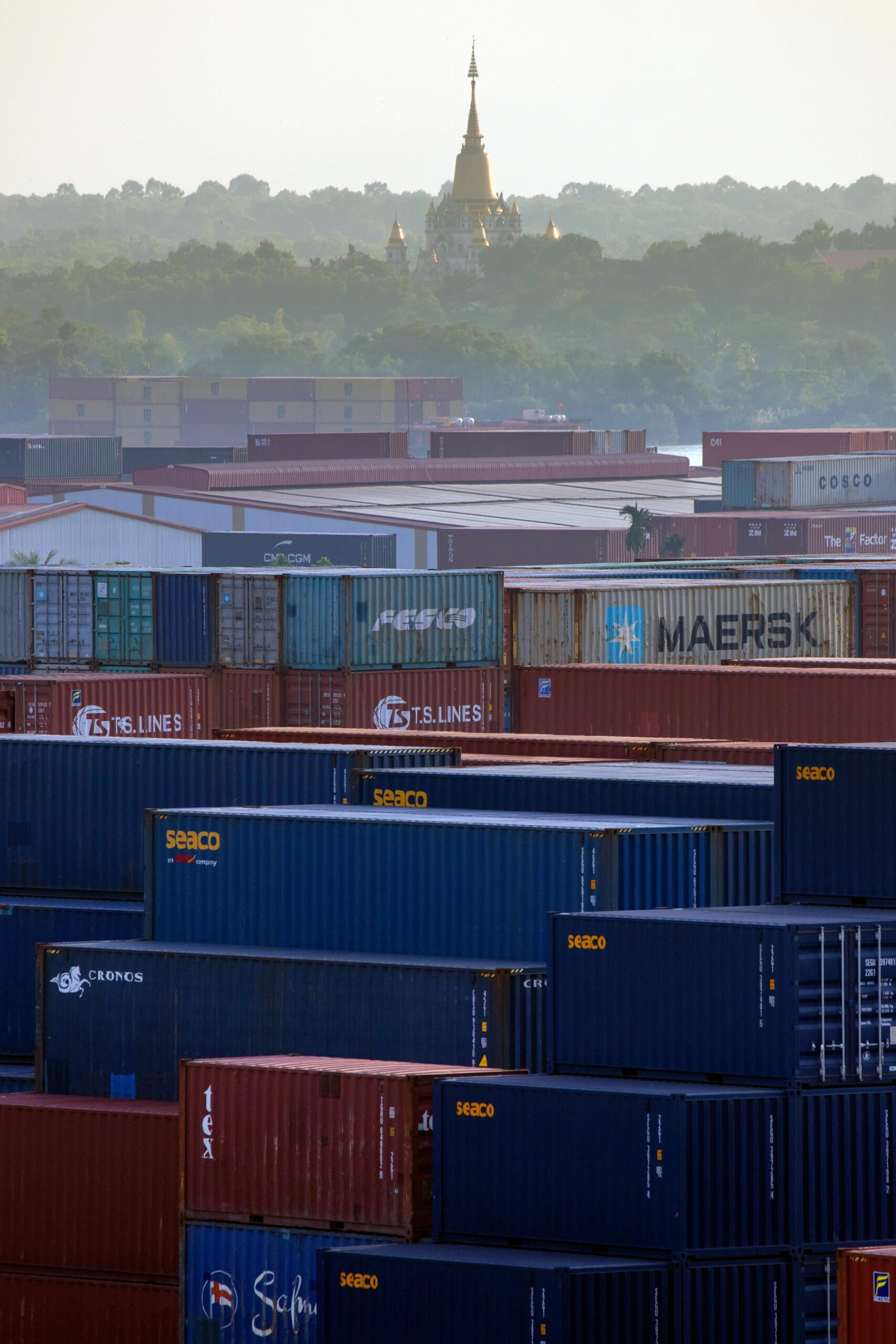 Vibrant shipping containers with a distant golden temple in a misty backdrop.